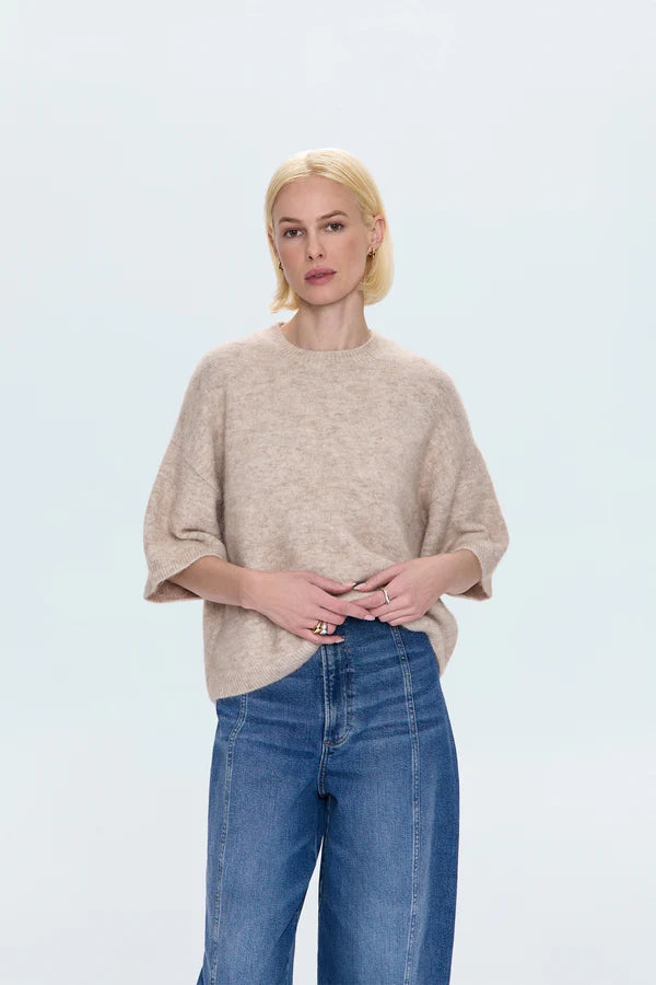 Woman wearing a beige sweater and blue jeans on a light gray background