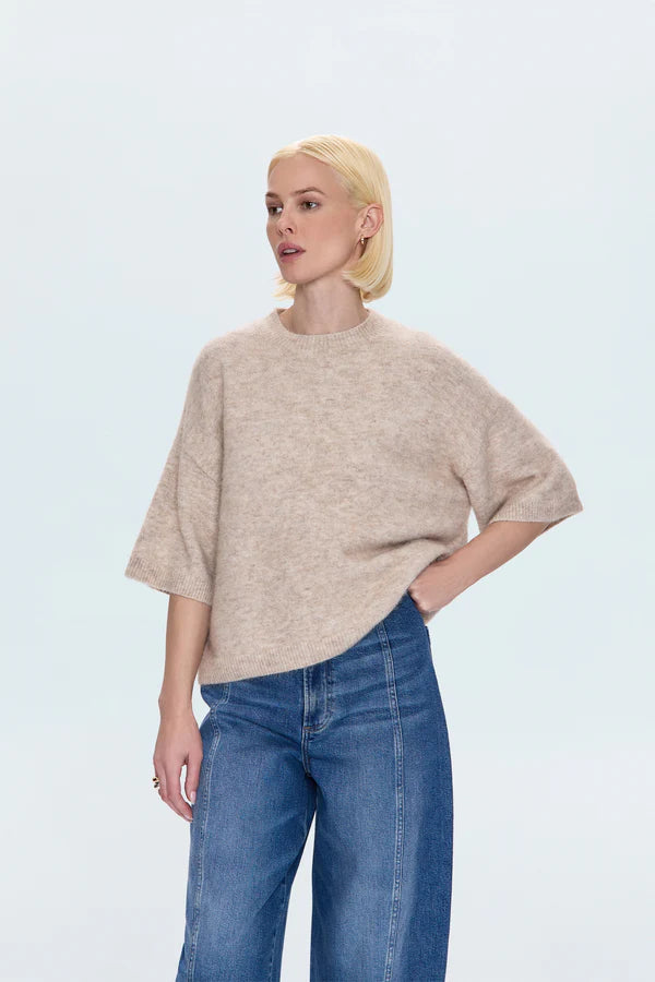 Woman wearing a beige sweater and blue jeans on a light gray background