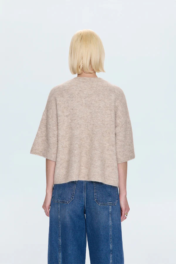 Person wearing a beige sweater and blue jeans on a light gray background