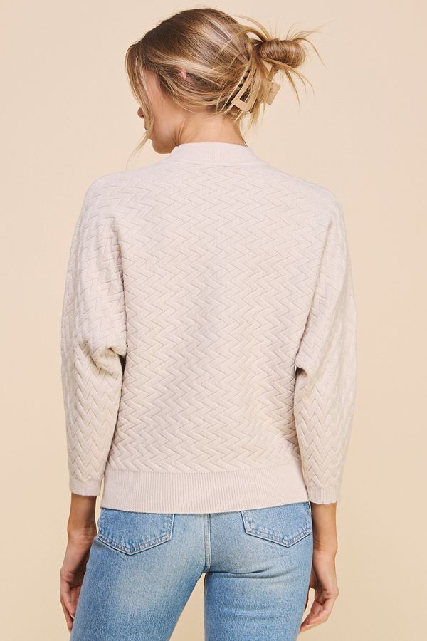 Person wearing a beige quilted sweater and blue jeans on a beige background