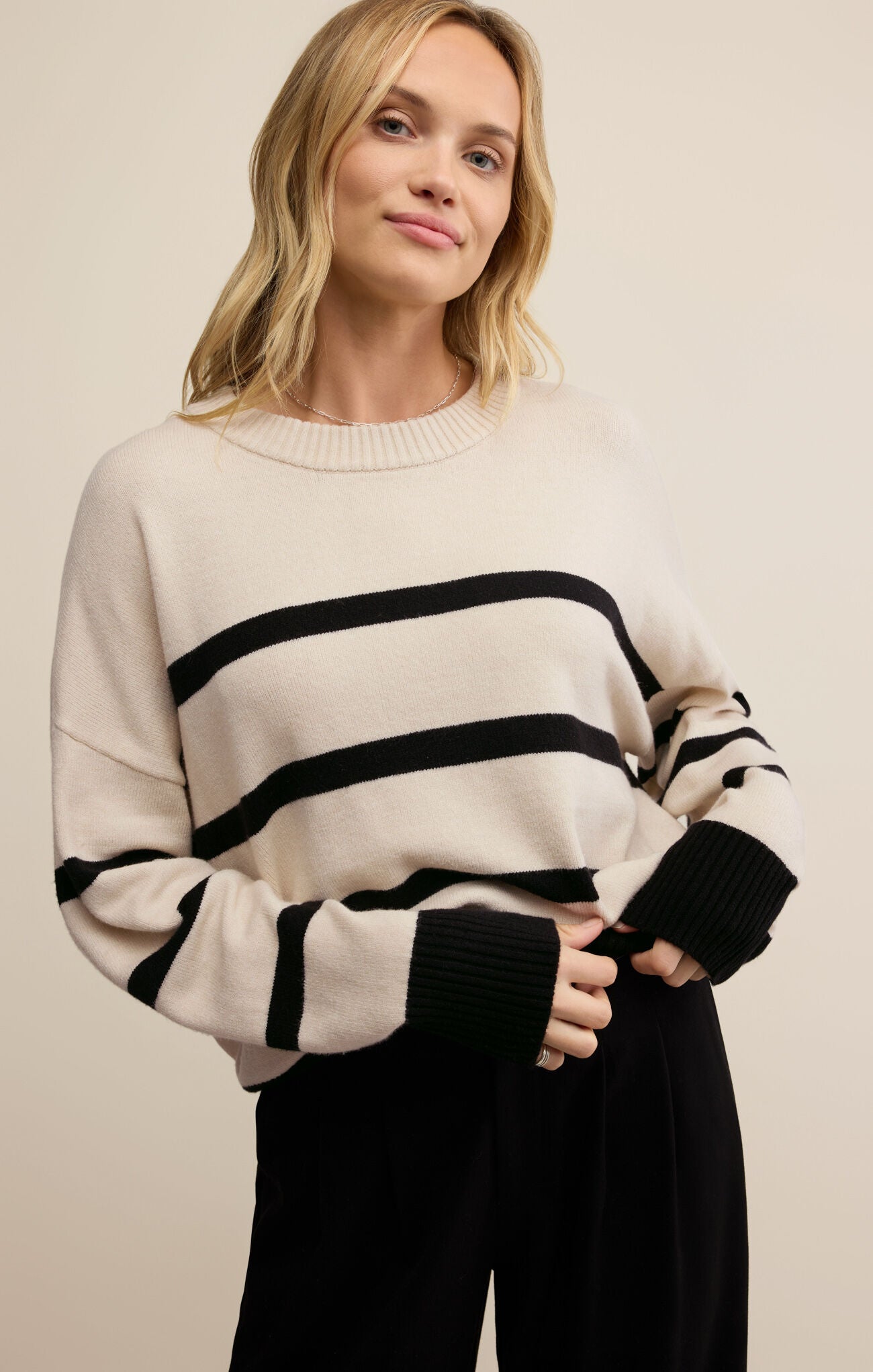 Woman wearing a cream sweater with black stripes on a beige background