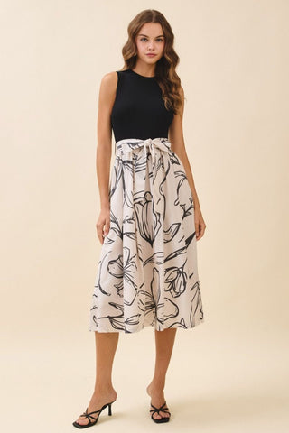 Woman wearing a black sleeveless top and white patterned skirt on a beige background