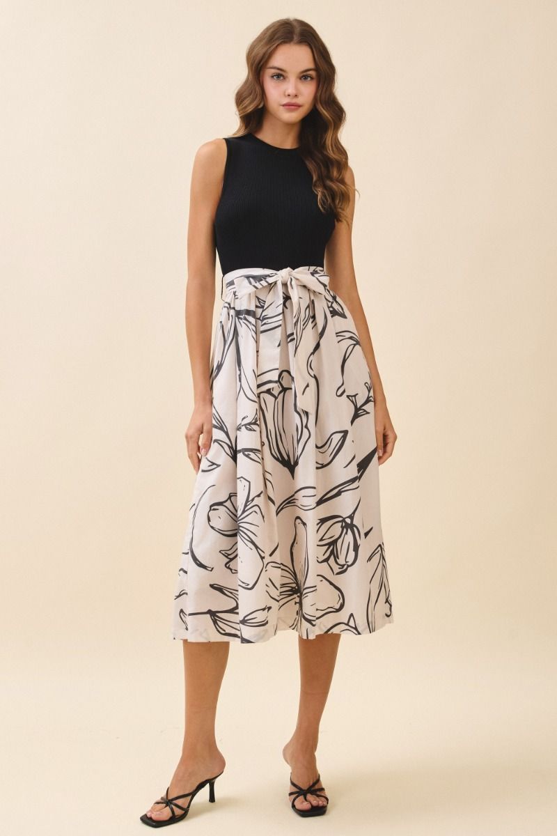 Woman wearing a black sleeveless top and white patterned skirt on a beige background