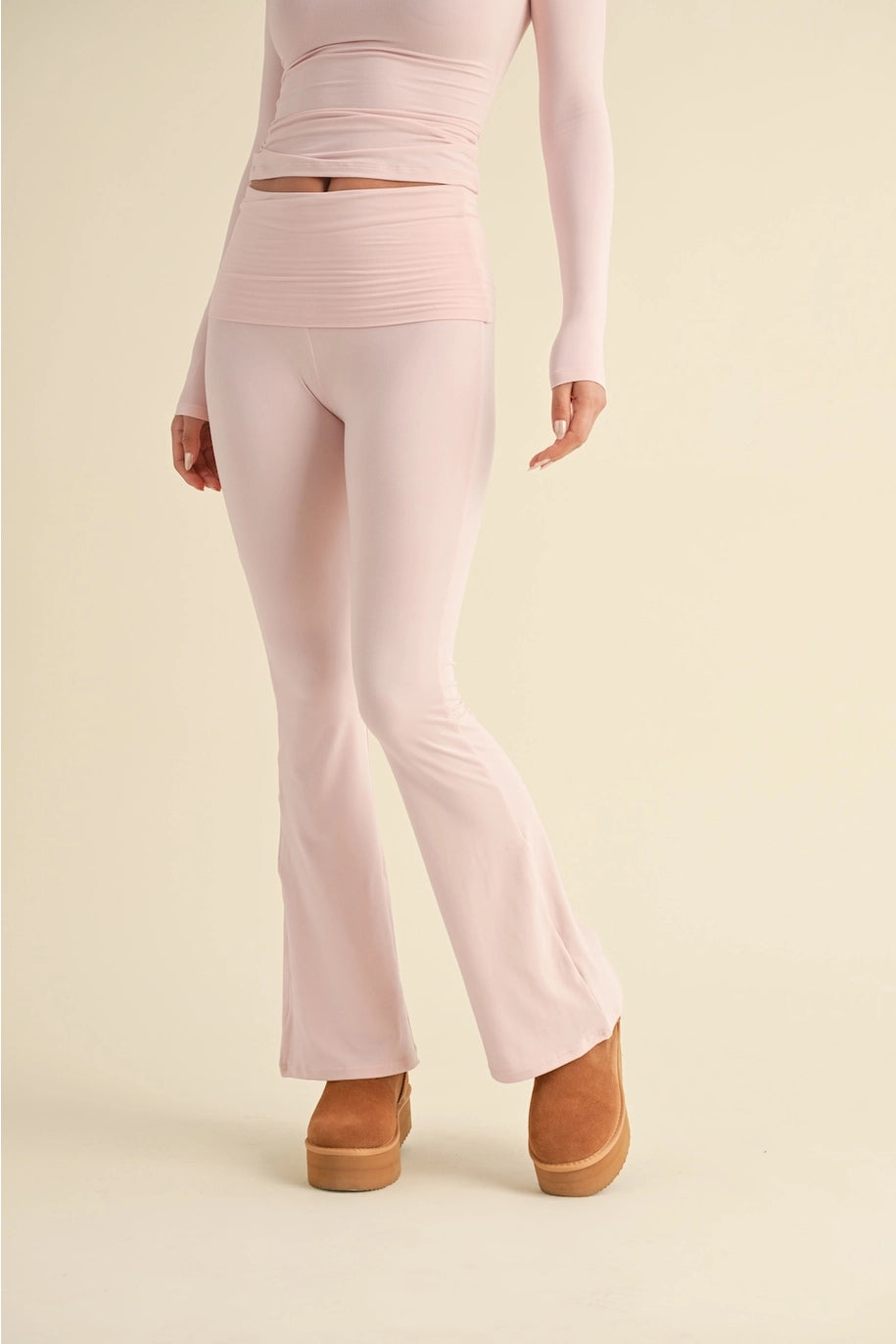 Person wearing light pink flared pants and a matching top on a beige background