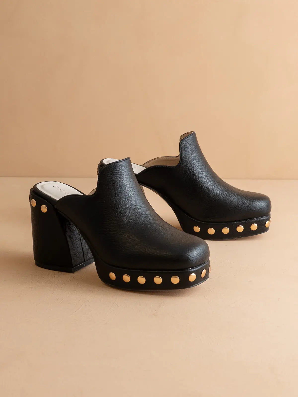 Black clogs with gold studs on a beige background