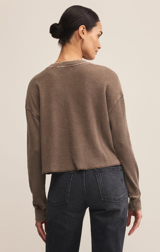 Woman wearing a brown textured sweater and dark jeans on a beige background