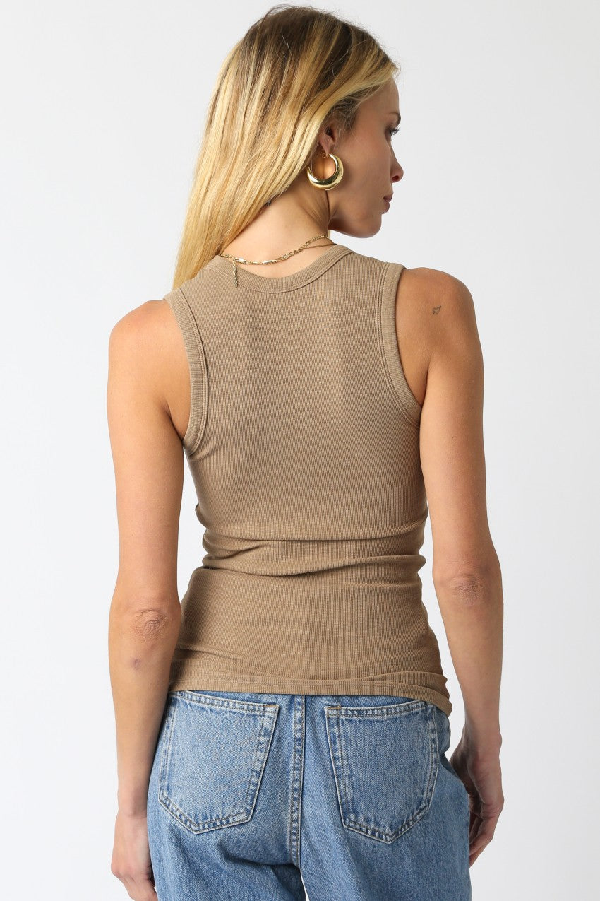 Person wearing a beige tank top and blue jeans on a white background