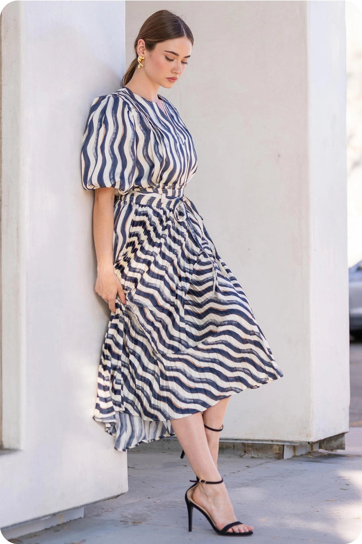 Woman wearing a blue and white striped dress against a white wall.