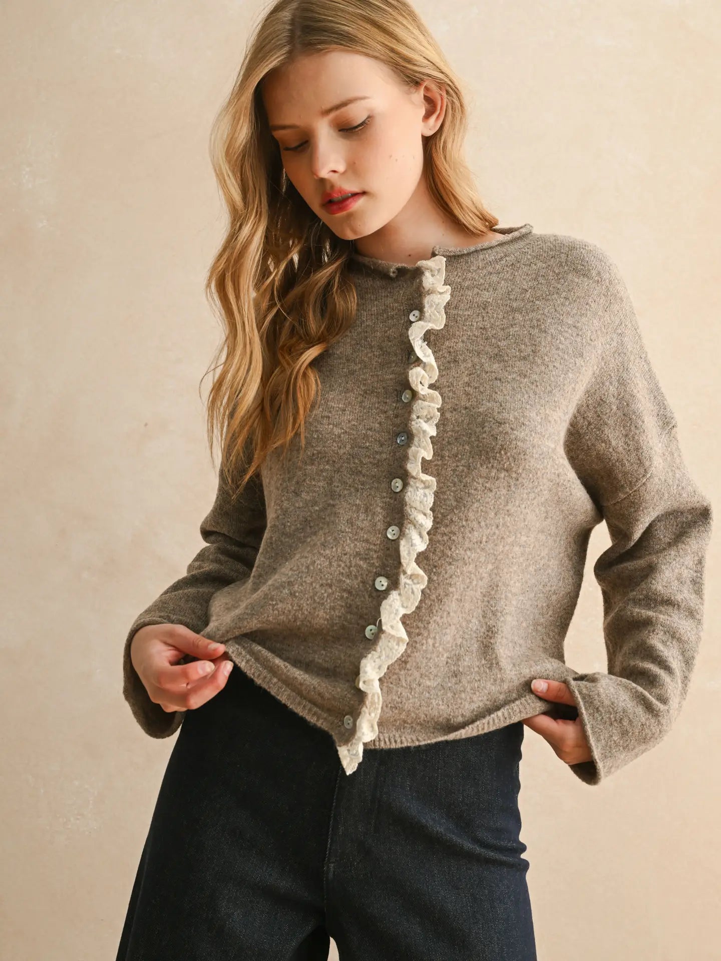 Woman wearing a brown sweater with ruffled details on a beige background
