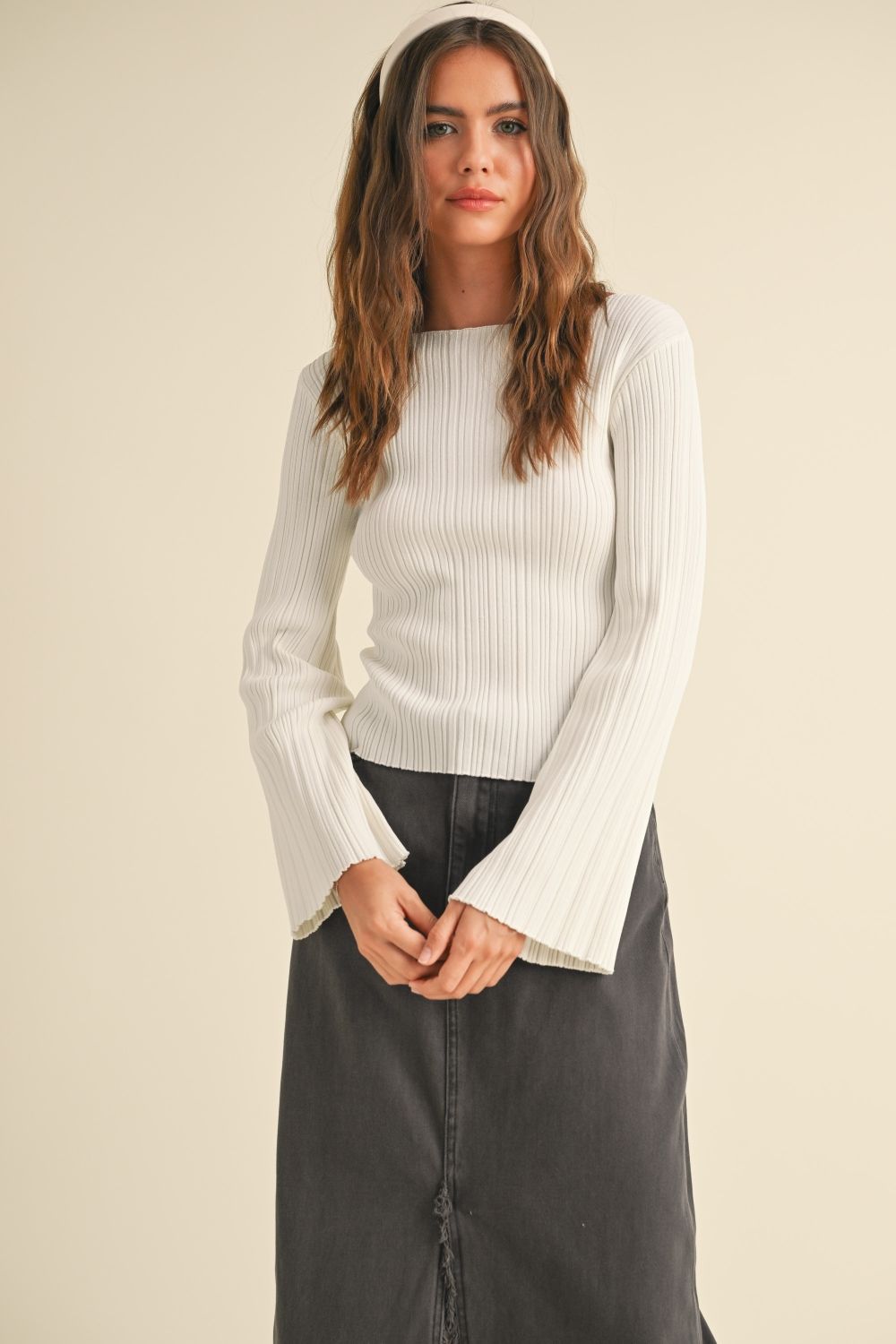 Woman wearing a white ribbed sweater over a black top on a beige background