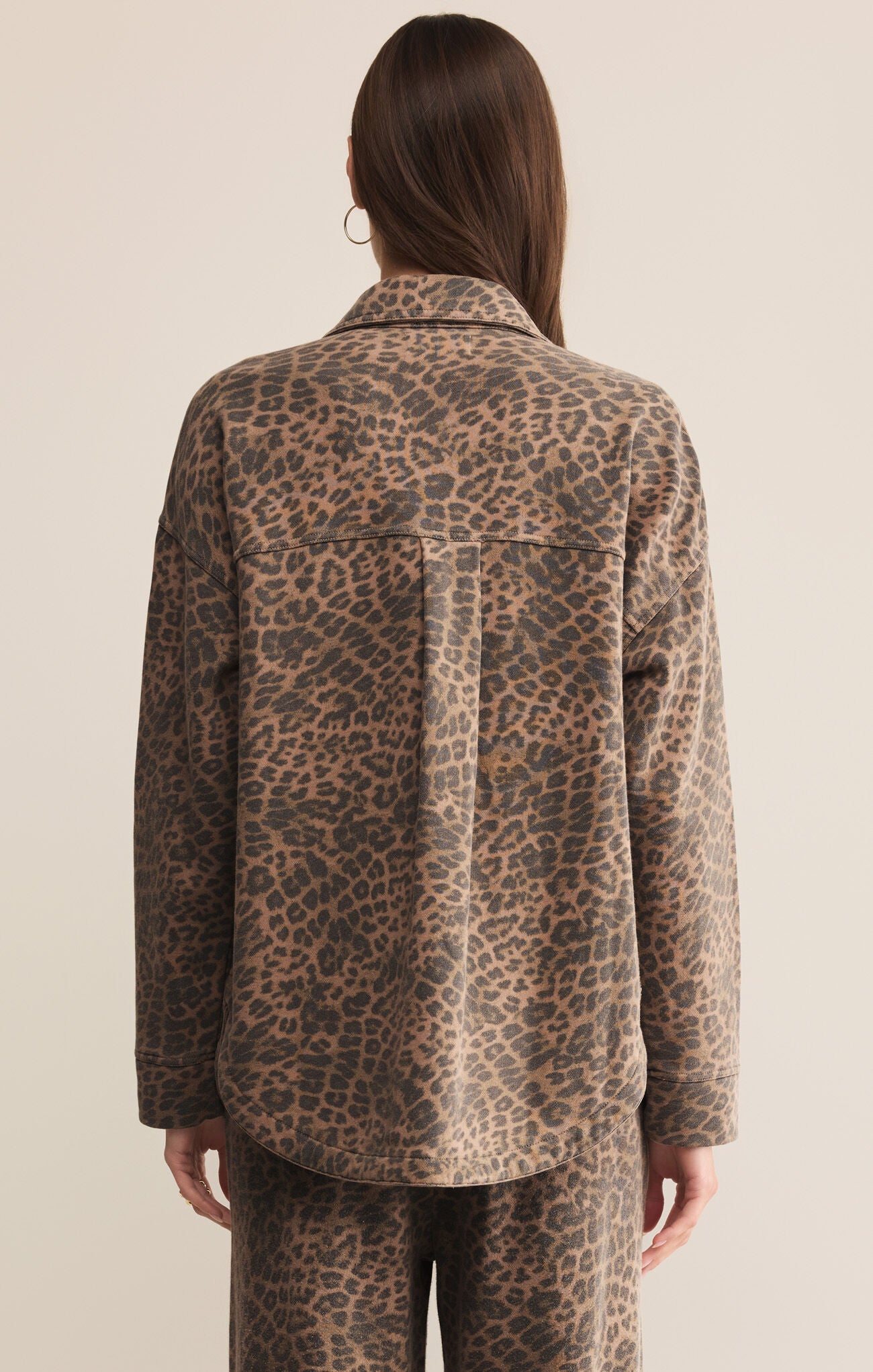 Person wearing a leopard print shirt and pants on a beige background