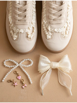 Beige sneakers with decorative lace, pearl accessories, and a bow on a beige background