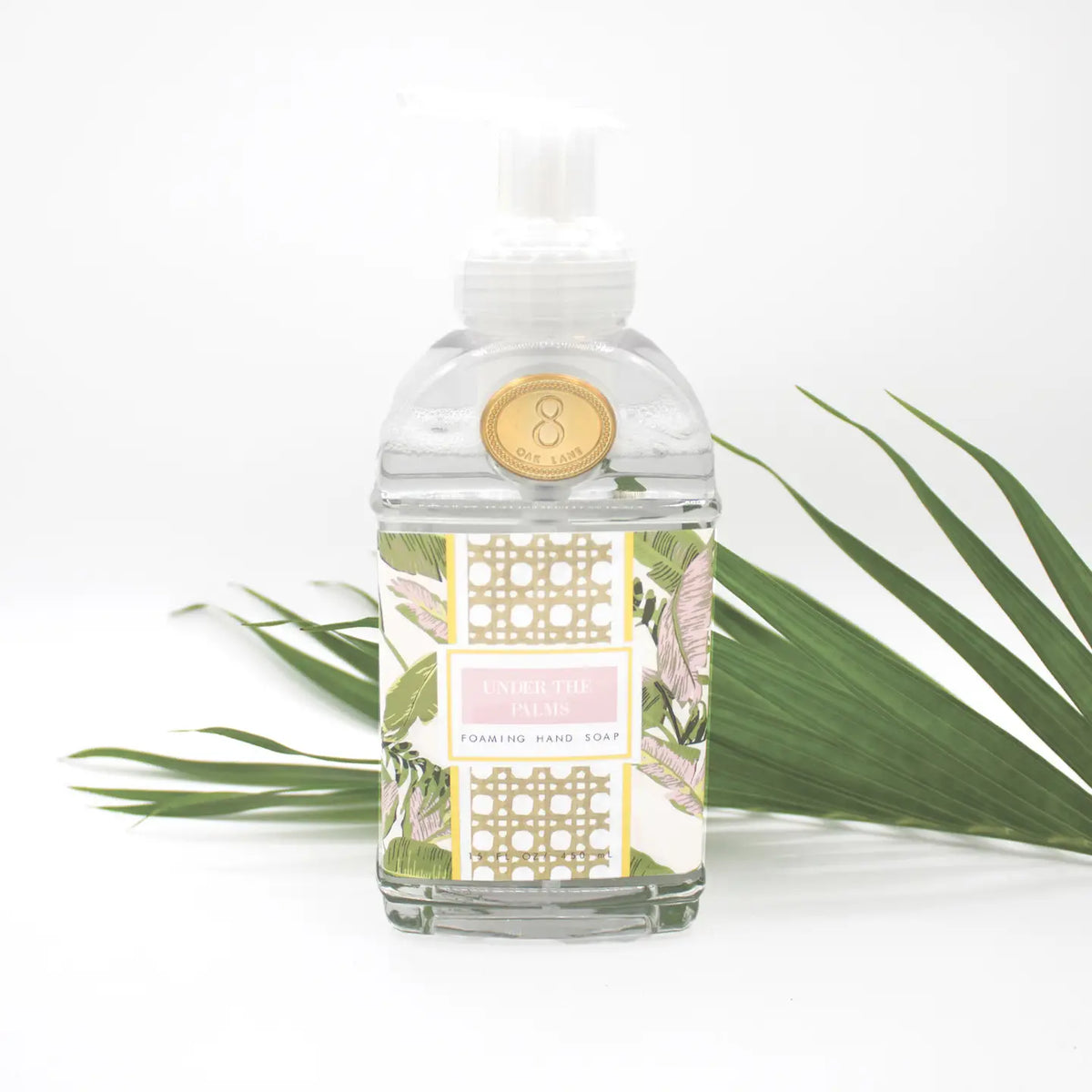 Clear bottle with decorative label and gold emblem on a white background with green leaves.