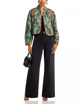 Person wearing a patterned jacket and black pants with a black handbag on a white background