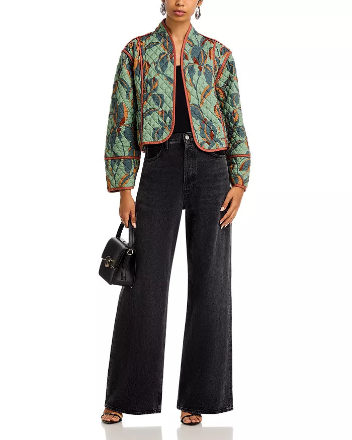 Person wearing a patterned jacket and black pants with a black handbag on a white background