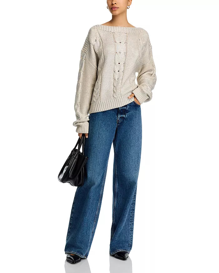 Woman wearing a beige cable knit sweater with blue jeans on a white background
