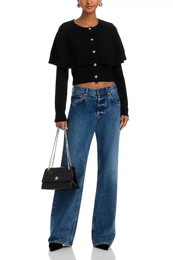 Person wearing a black cropped cardigan with silver buttons and blue jeans on a white background