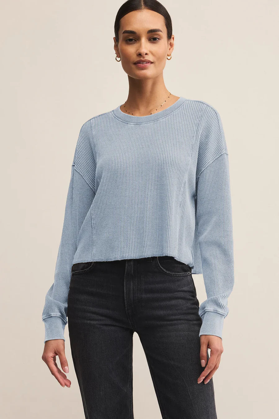 Woman wearing a light blue ribbed sweater and black pants on a beige background