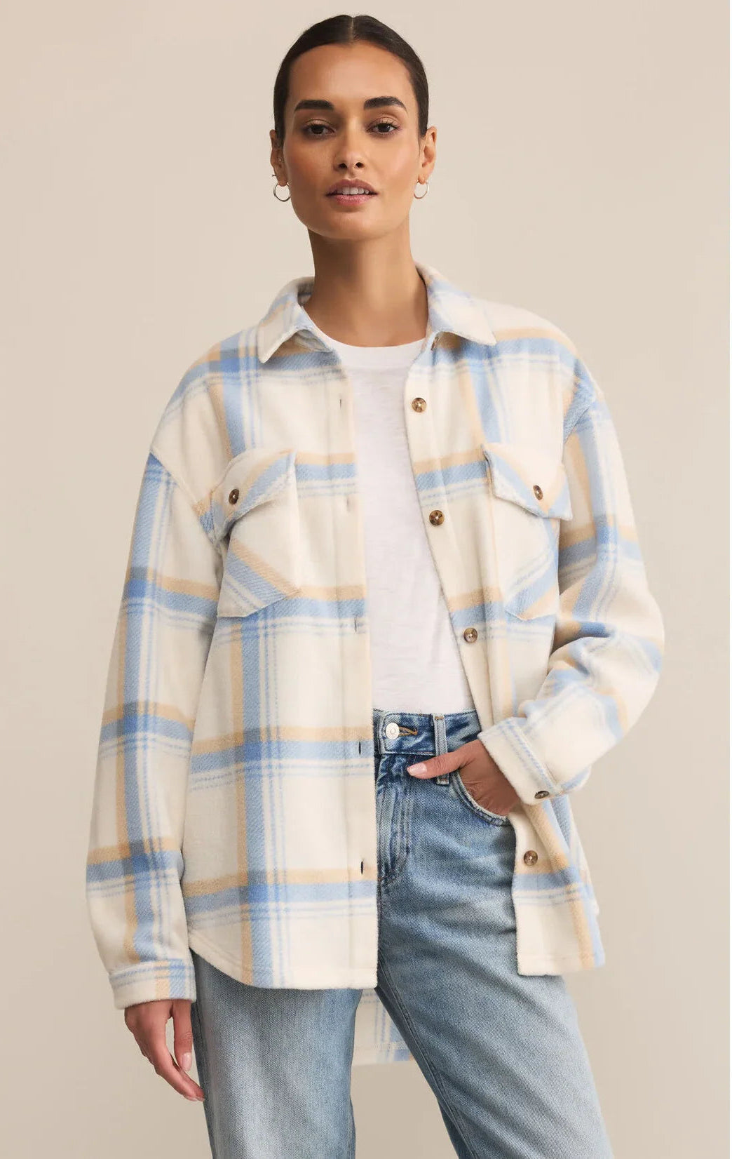 Woman wearing a plaid shirt over a white top and jeans on a beige background