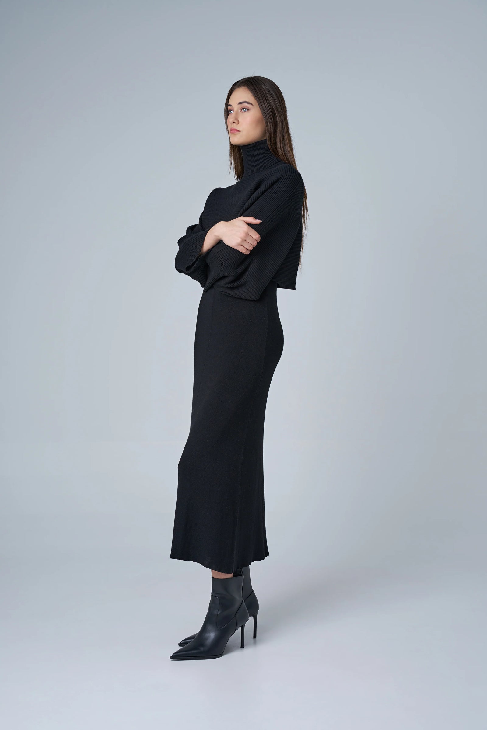 Woman wearing a black outfit with a turtleneck top and skirt on a white background