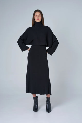 Woman wearing a black outfit with a turtleneck top and skirt on a white background