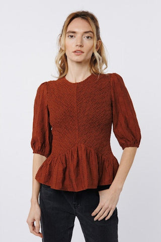 Woman wearing a rust-colored peplum top against a white background