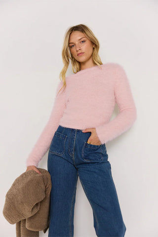 Woman wearing a pink sweater and blue jeans against a white background