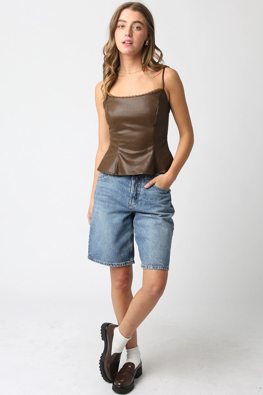 Woman wearing a brown leather top and blue denim shorts on a white background