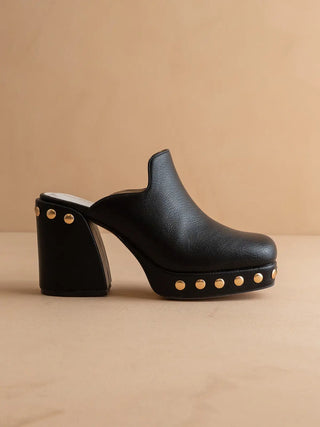 Black clog shoe with gold studs on a beige background