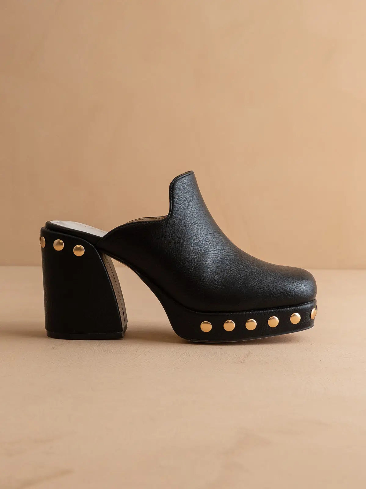 Black clog shoe with gold studs on a beige background