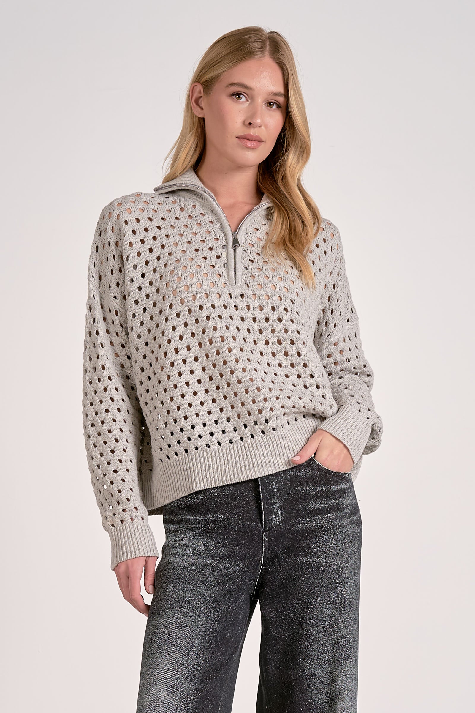 Woman wearing a beige patterned sweater with a quarter zip and jeans on a white background