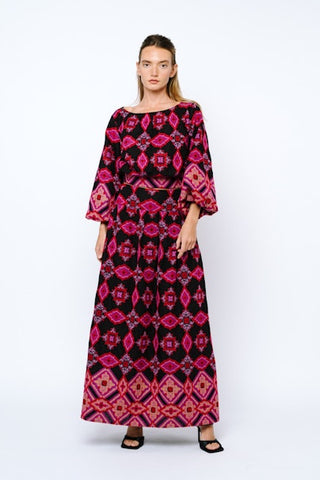 Woman wearing a long, patterned dress with pink and black design on a white background