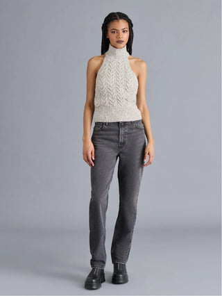 Woman wearing a cream knitted top and gray jeans on a gray background