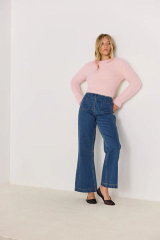 Woman wearing a pink sweater and blue jeans against a white background