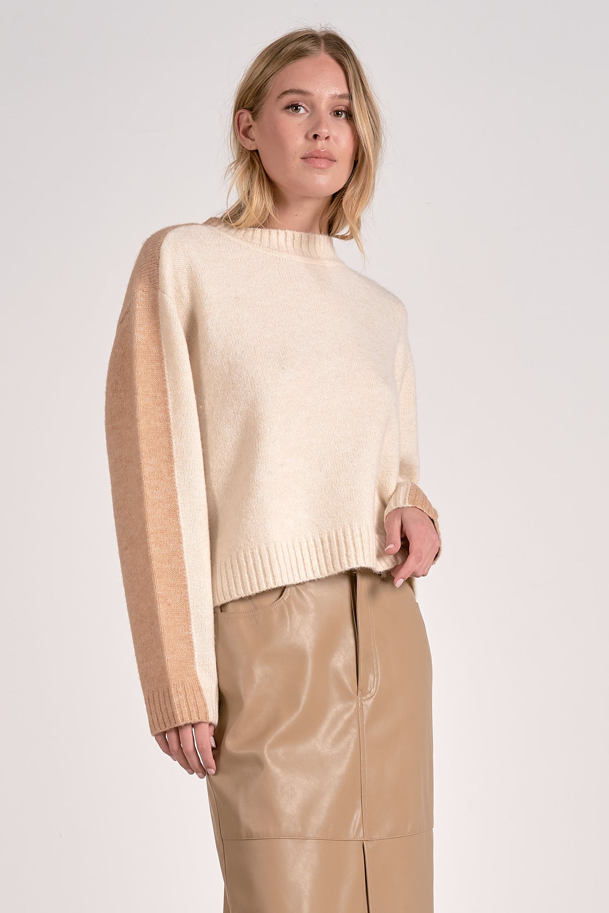Woman wearing a beige sweater and pants against a white background