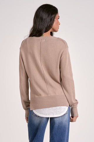 Woman wearing a beige sweater and blue jeans on a plain background