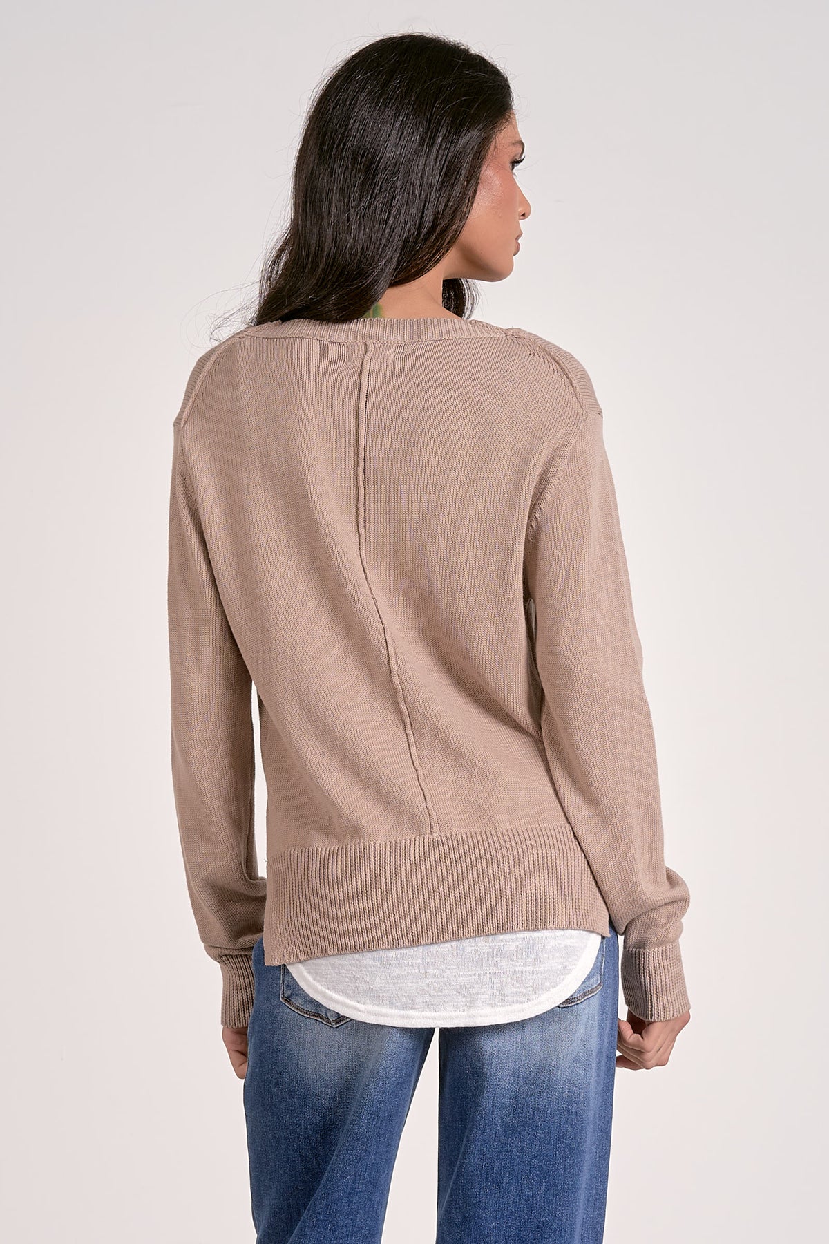 Woman wearing a beige sweater and blue jeans on a plain background