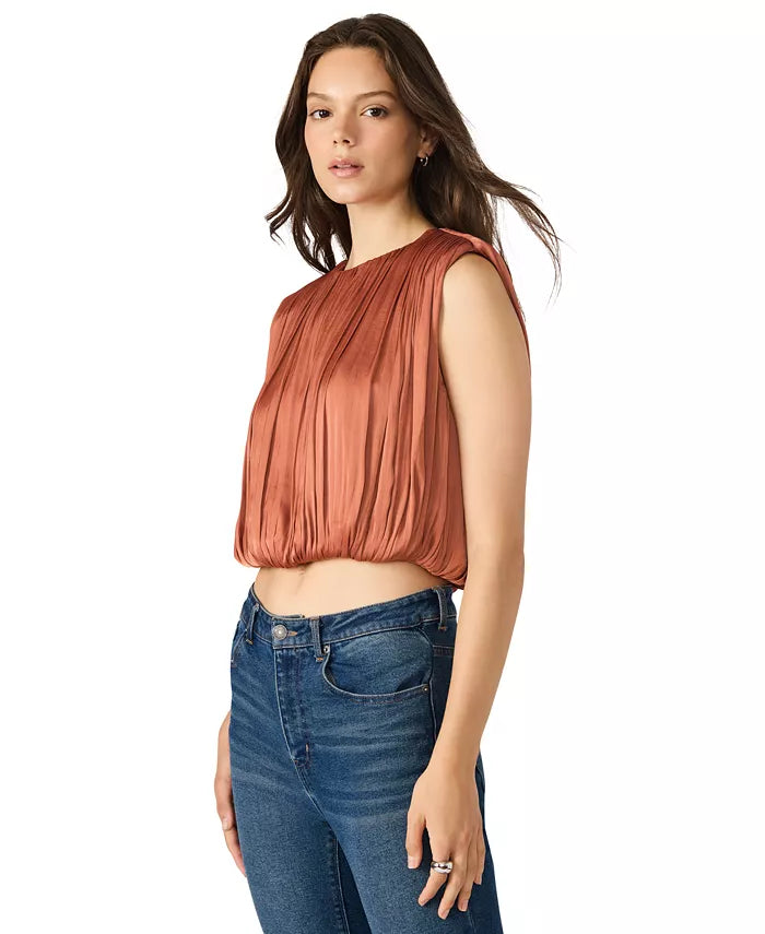 Woman wearing a rust-colored sleeveless top and blue jeans on a white background