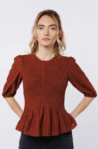 Woman wearing a rust-colored textured blouse with puffed sleeves on a white background