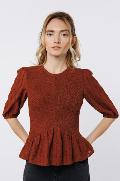 Woman wearing a rust-colored peplum top against a white background