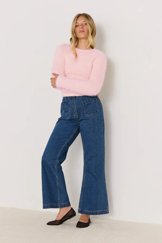 Woman wearing a pink sweater and blue jeans against a white background