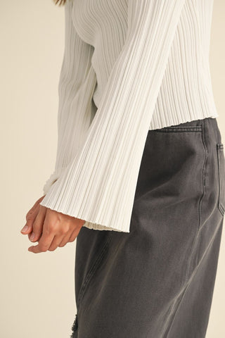 Person wearing a white ribbed sweater and dark pants on a beige background