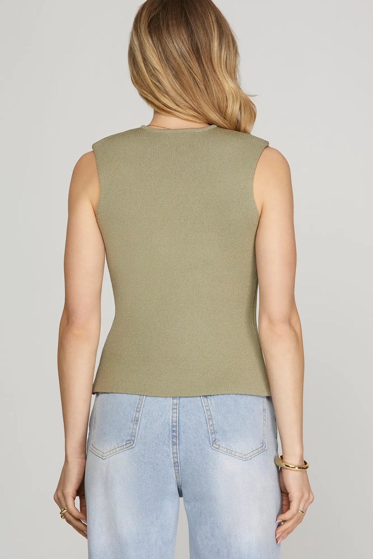 Person wearing a green sleeveless top and light blue jeans on a plain background