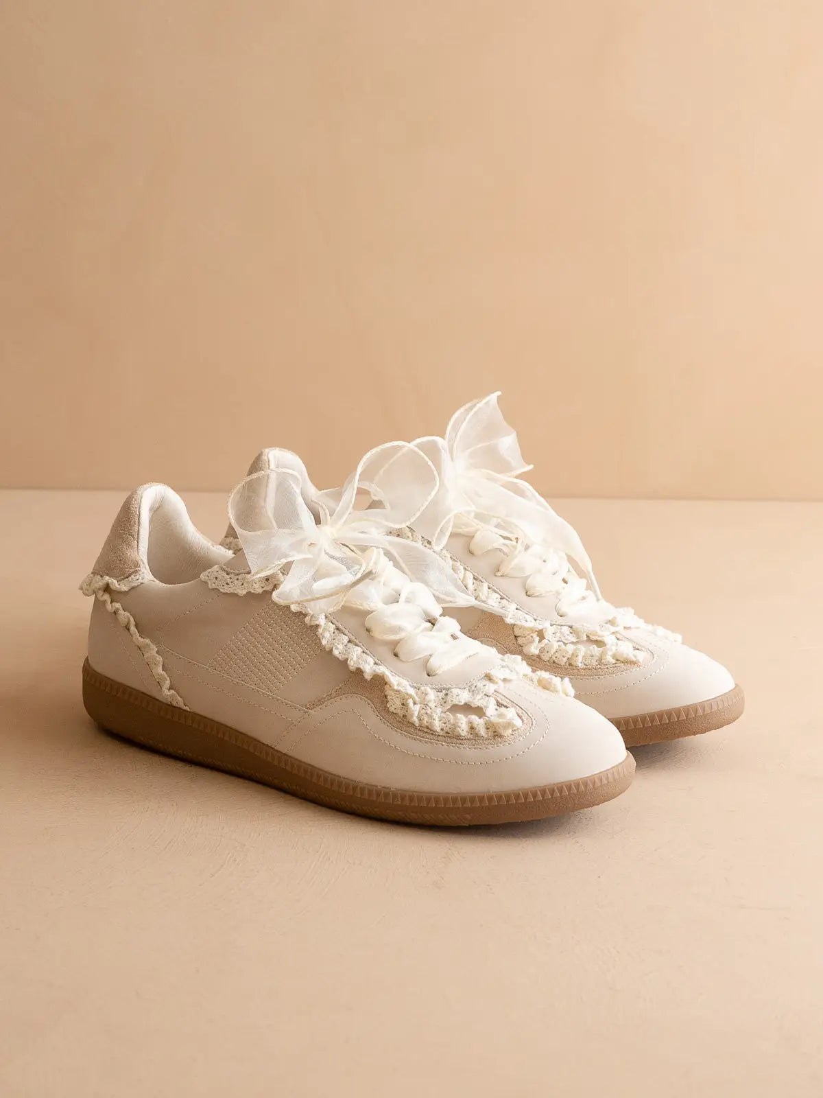 Pair of white sneakers with lace and pearl details on a beige background