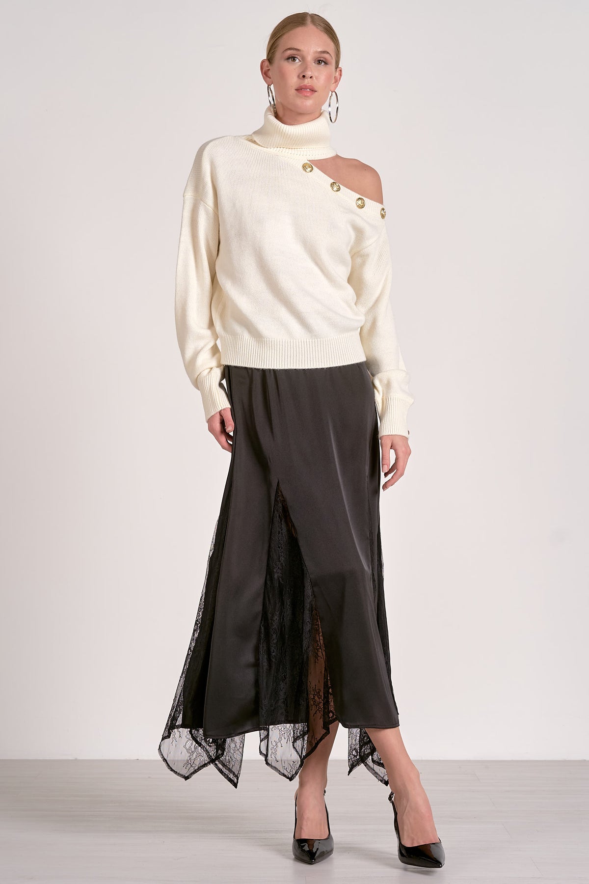 Woman wearing a cream sweater with a cut-out design and a black skirt on a white background