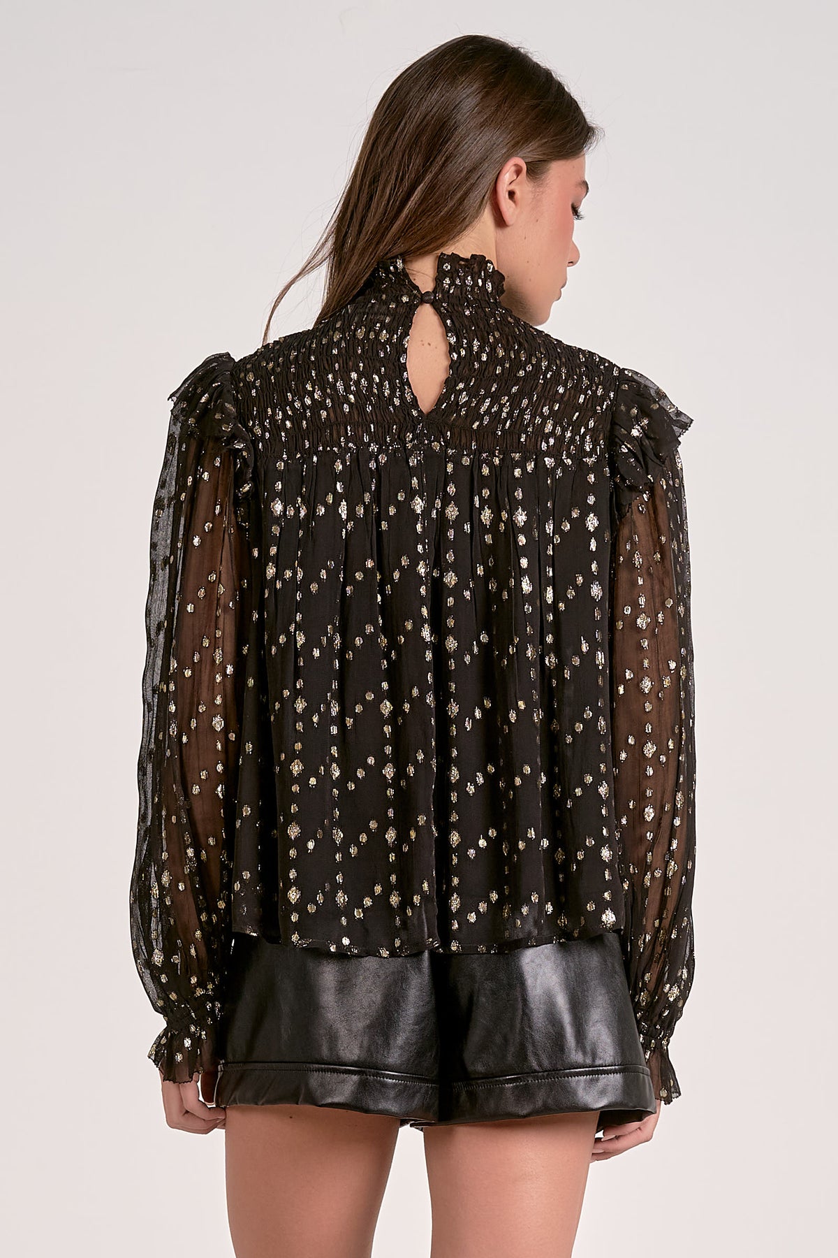 Woman wearing a black blouse with sheer sleeves and a cut-out back design on a white background