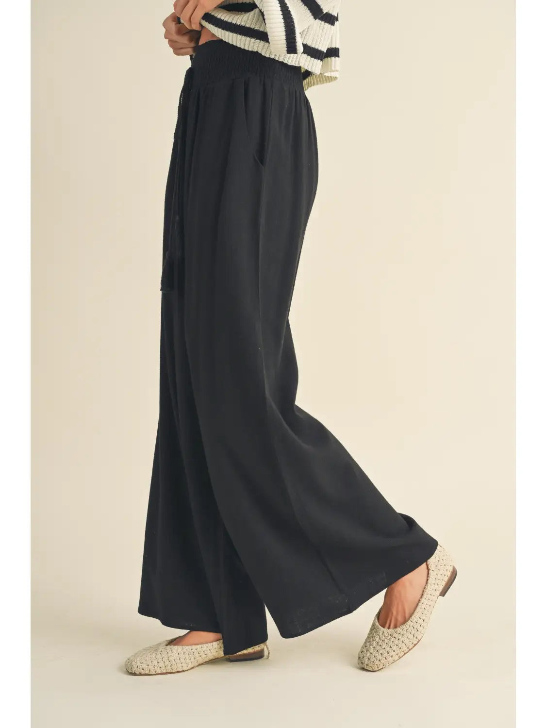 Person wearing wide-leg black pants on a beige background