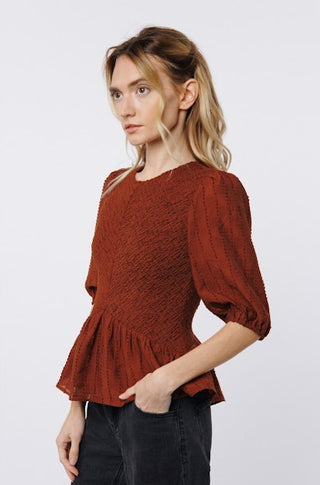 Woman wearing a rust-colored textured blouse against a white background