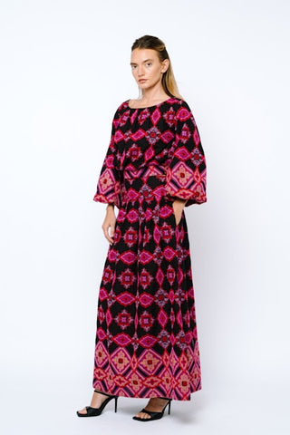 Woman wearing a long, patterned dress with bell sleeves on a white background