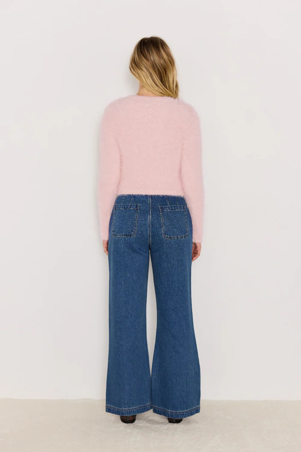 Person wearing a pink sweater and blue jeans on a white background